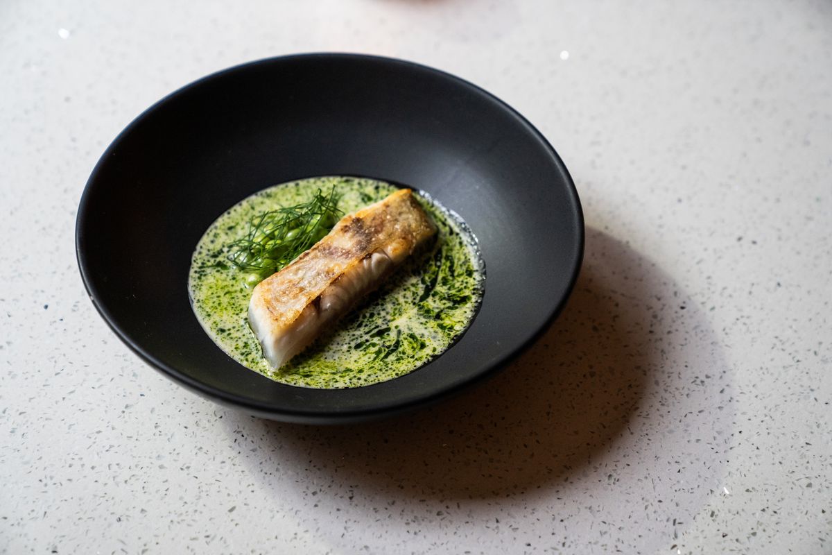 A black bowl with green sauce and grilled seabass.