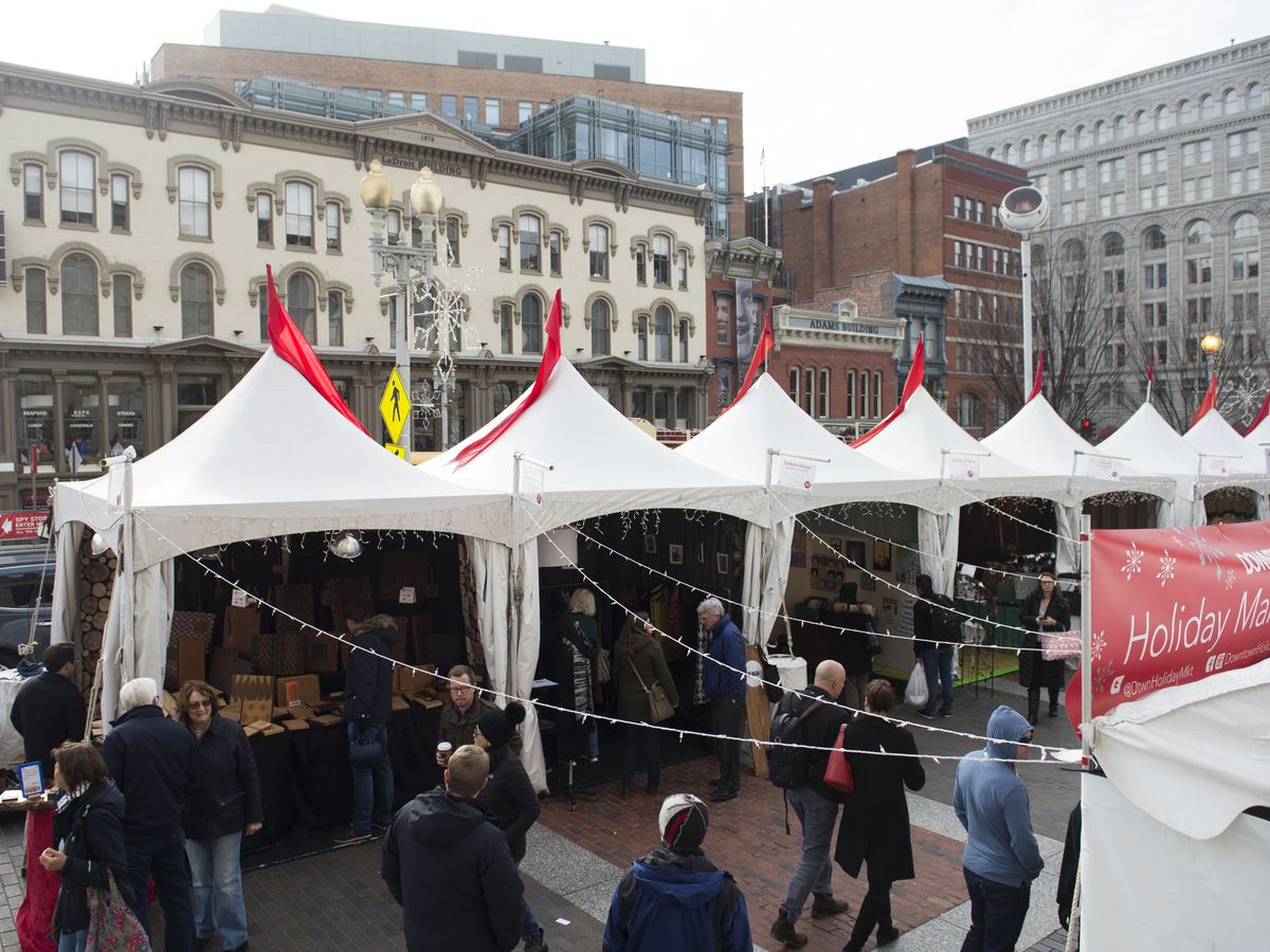 A holiday market with white tents in a downtown area. People browse and mill about.