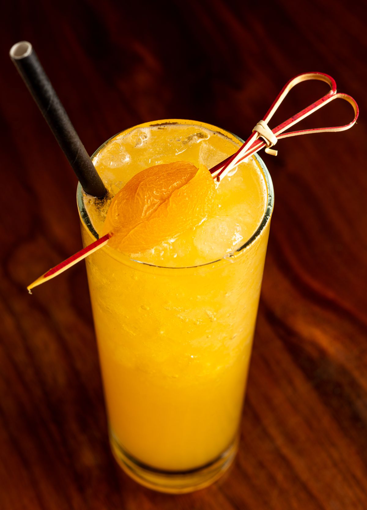 A tall glass shown from above with an apricot-colored cocktail topped by a skewered apricot. 