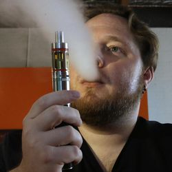 In this photo taken Thursday, July 16, 2015, Bruce Schillin, 32, exhales vapor from an e-cigarette at the Vapor Spot, in Sacramento, Calif.  As e-cigarettes rise in popularity, "vape shops" are popping up around the nation, places where customers can gather to inhale doses of nicotine through a flavored vapor solution. Industry officials say California is at the epicenter, with an estimated 1,400 retailers, operating largely without regulations in a Wild West atmosphere, but rules are imminent.  (AP Photo/Rich Pedroncelli)