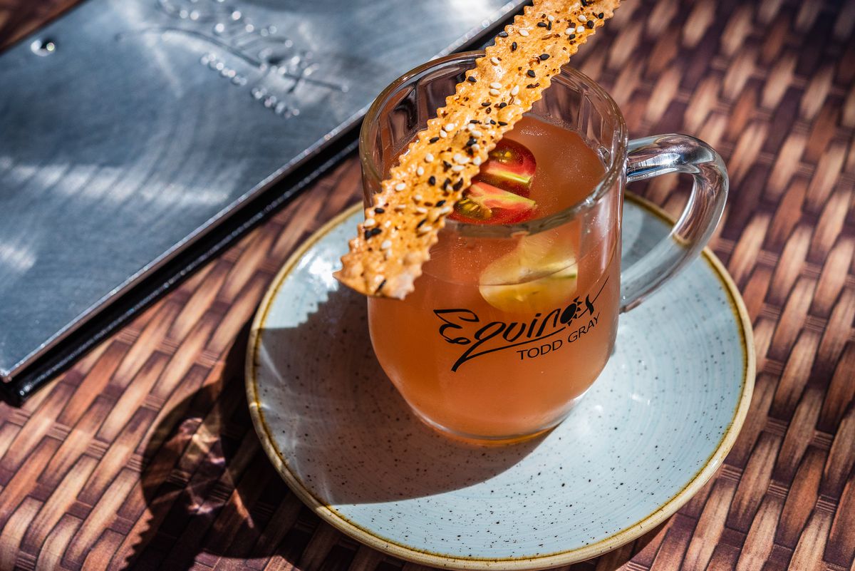 A glass of cold tomato pulp consomme topped with a sesame lavash cracker from Equinox.