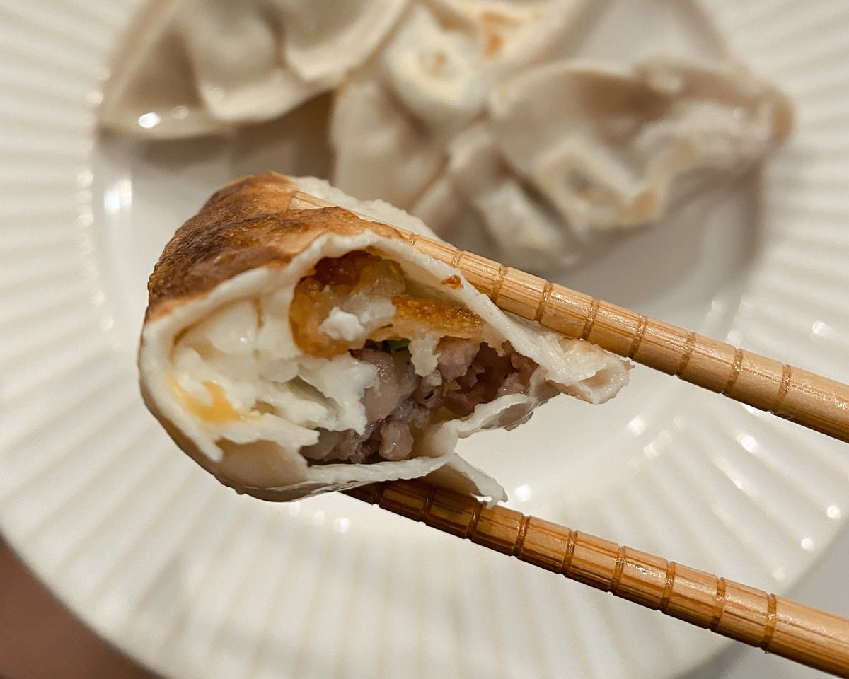 chopsticks hold a bitten-into dumpling.