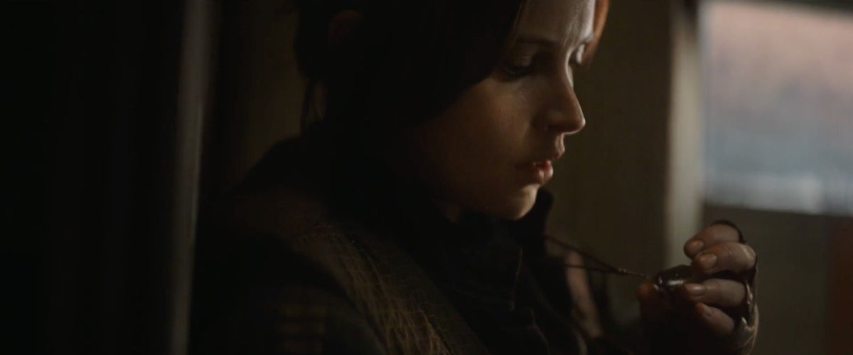 Jyn Erso, looking over her kyber pendant. 