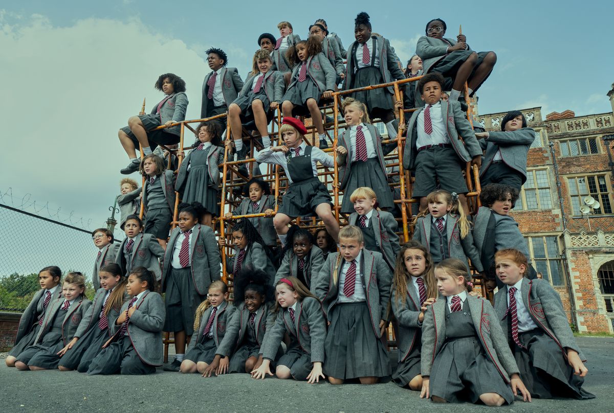 The school children in Matilda the Musical stack on a playground wearing their school uniforms.