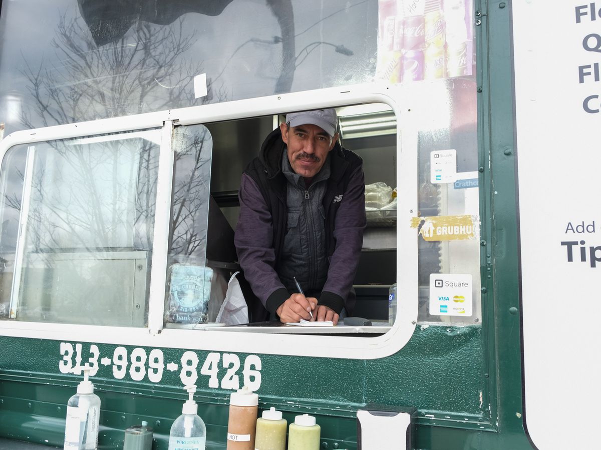 A man with a dark mustache looks through a window from the inside of the Tacos el Caballo food truck in southwest Detroit, Michigan.