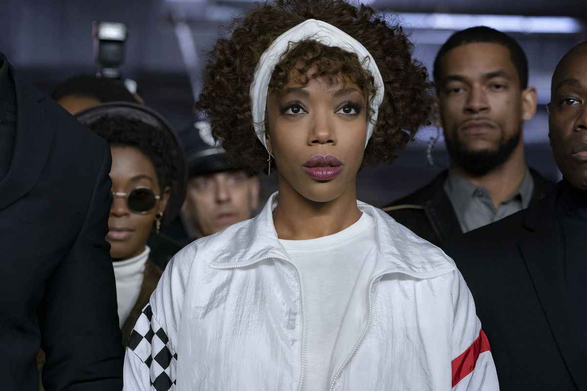 Naomi Ackie wears all white, with a white headband, and is surrounded by security guards as Whitney Houston in I Wanna Dance With Somebody.