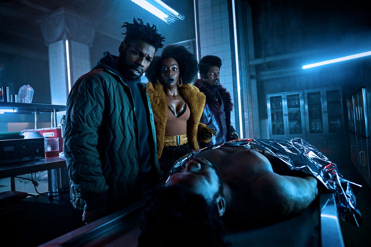 (L to R) John Boyega as Fontaine, Teyonah Parris as Yo-Yo and Jamie Foxx as Slick Charles staring down at a dead body on an examination table in They Cloned Tyrone.