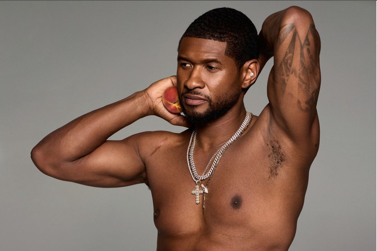 Usher posing shirtless with his arms behind his head, holding a peach.