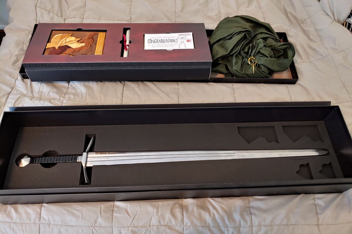 A box of Elden Ring goodies — including a whole-ass sword — sits on a bed