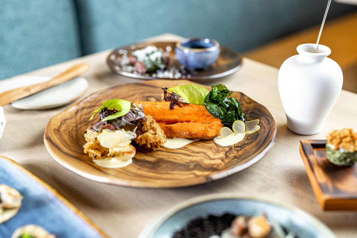 Amid a table of dishes, a bright orange salmon stands out on a wooden plate.