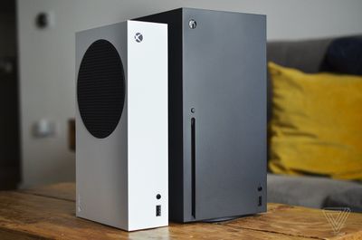 Microsoft’s white Xbox Series S sits alongside a bigger black Xbox Series X on a wooden coffee table in a living room
