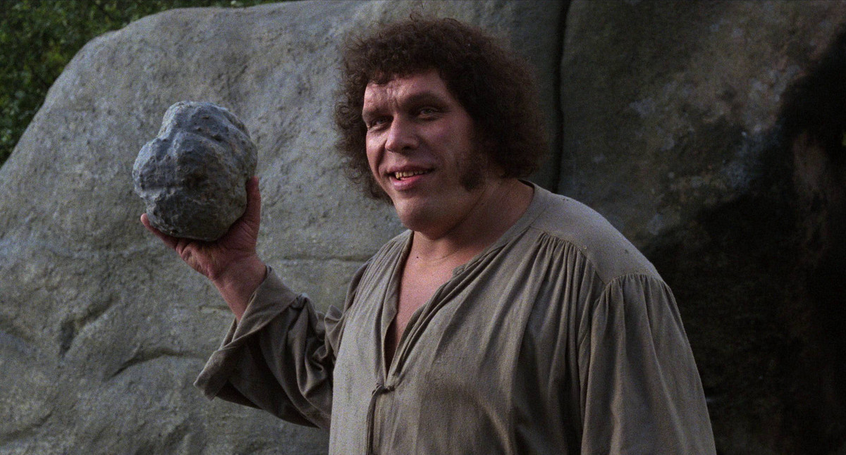 Andre the Giant holds a large rock while smiling in The Princess Bride.