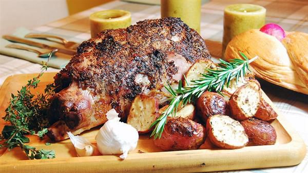 A large roast on a cutting board with sliced potatoes and herbs