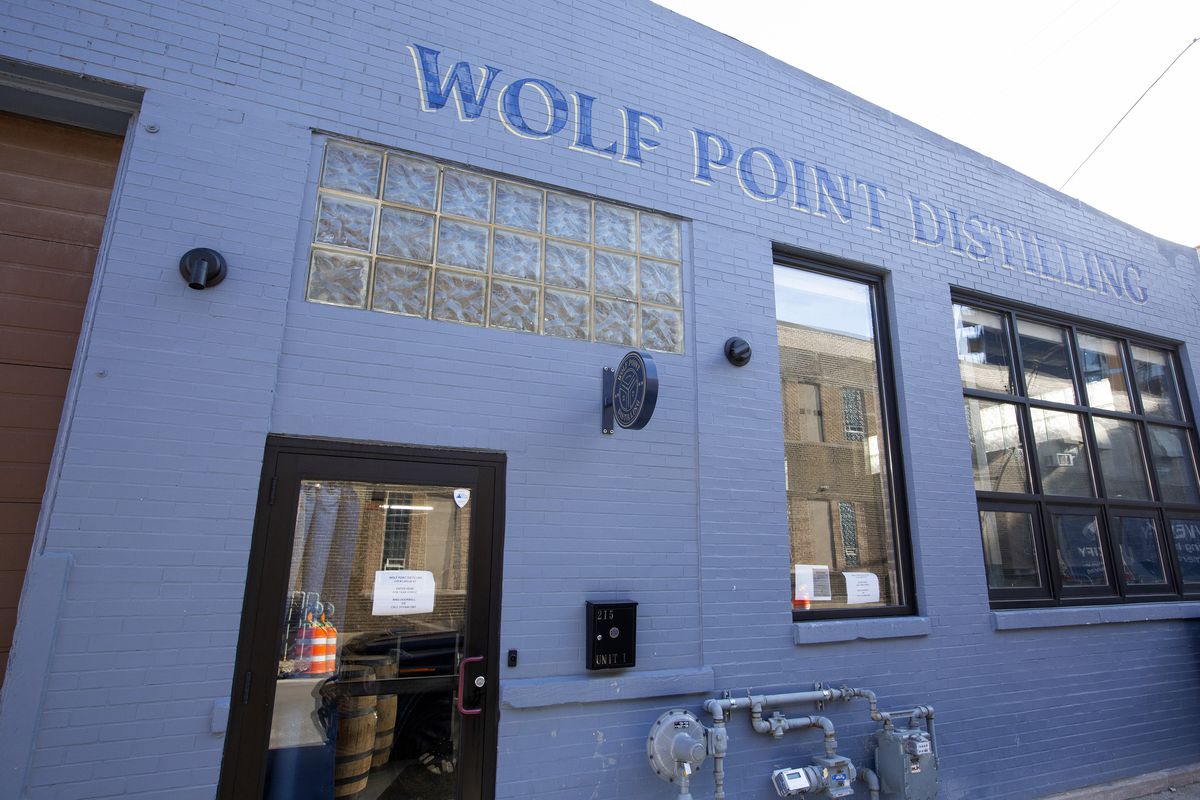 A blue-grey warehouse entrance with a painted sign that reads “Wolf Point Distilling”