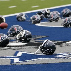 Several Houston Texans helmets sit over the Dallas Cowboys logo in the end zone as the Texans prepare for a morning work out at the Cowboys training facility, Monday, Aug. 28, 2017, in Frisco, Texas. The Texans are working out in the practice facility of the Cowboys because of floods pounding Houston. An exhibition game in the Texans' stadium Thursday might be moved to the home of the Cowboys.