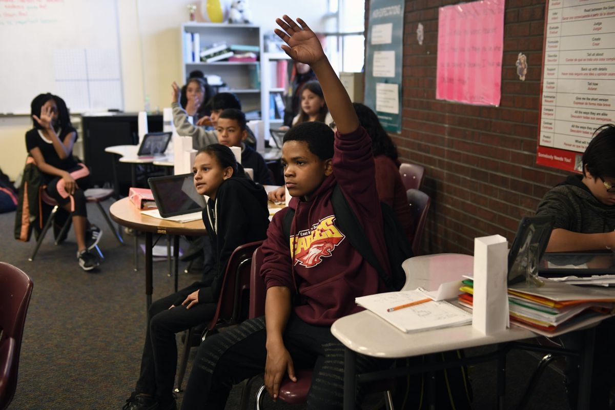 Russell Patton, hand raised high, waits to be called on during Ines Barcenas’ sixth grade math class in March 2018 at East Middle School in Aurora.