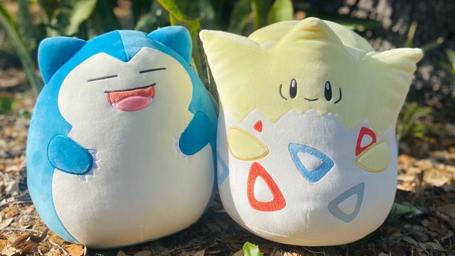 Snorlax and Togepi in Squishmallow form, placed on the ground outside in front of some plants.