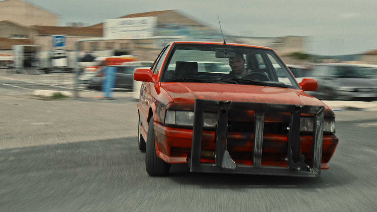 Alban Lenoir como Lino dando la vuelta a una esquina en su muscle car rojo en Lost Bullet.