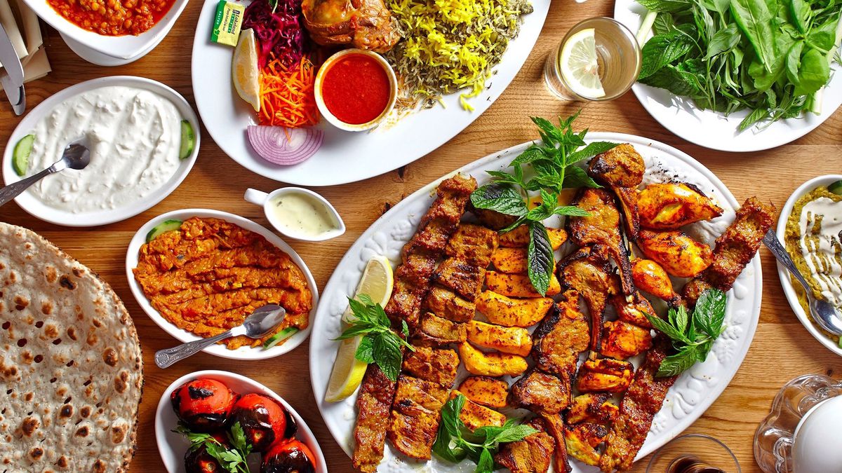 An overhead shot of a table of varied foods including meat kabobs, bread, rice, and roasted chicken.