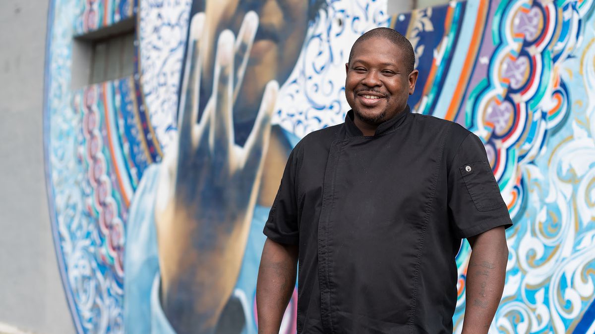 A male chef with a black coat stands in front of a colorful mural at a Los Angeles restaurant.