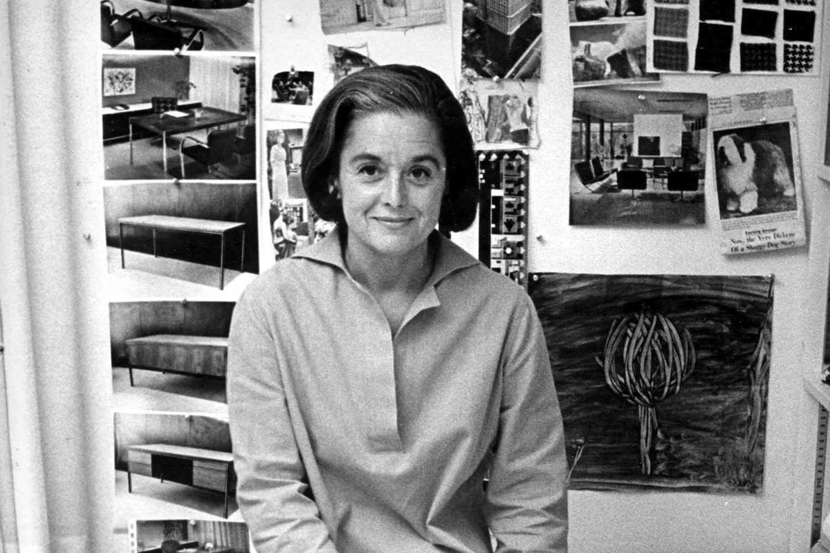 Portrait of American architect and furniture designer Florence Knoll Bassett as she sits on the edge of a table with a book of fabric swatches in front of her, 1961.