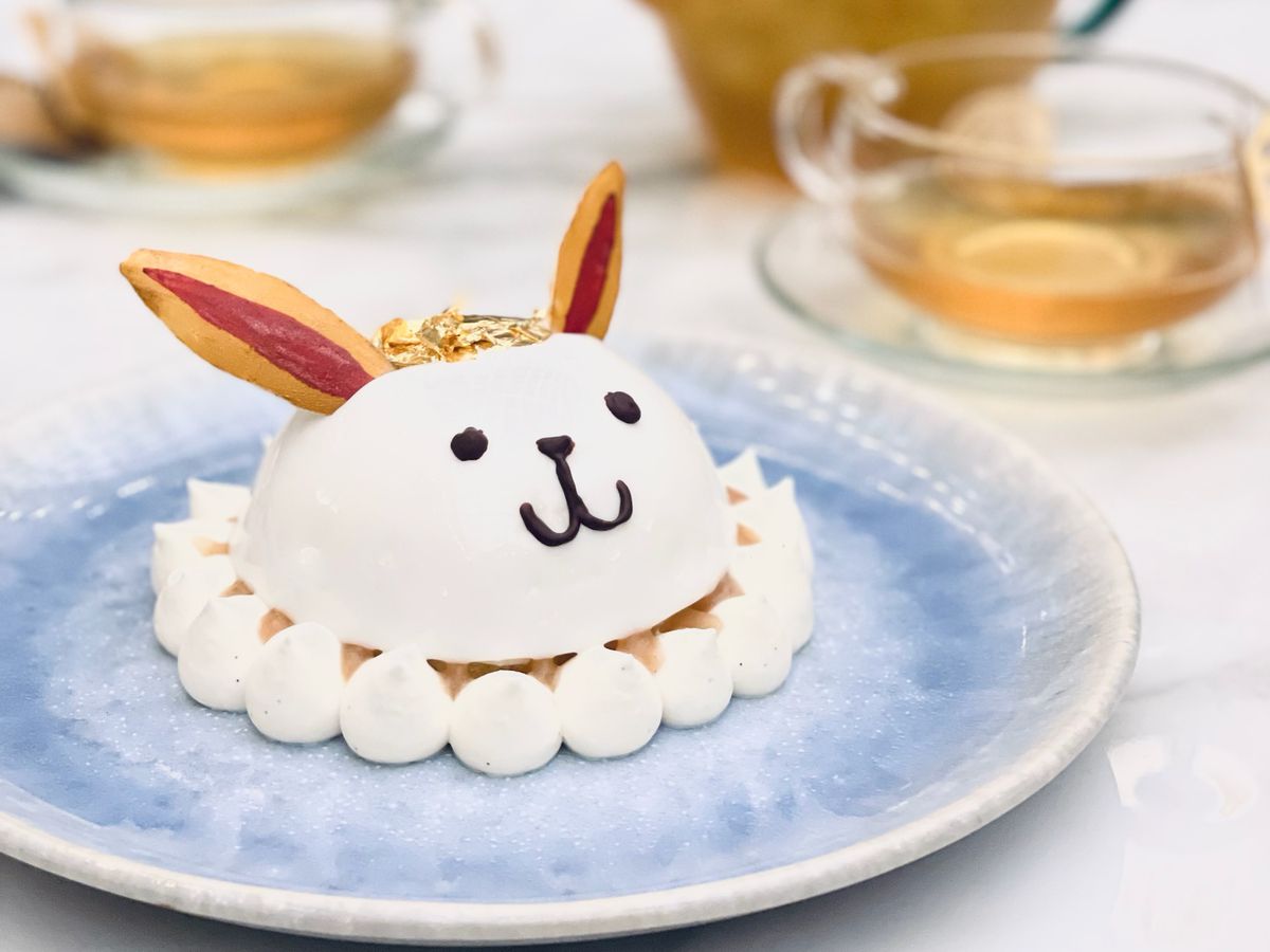 A dome-shaped cake with a rabbit face and ears sits on a small circular plate with teacups and a teapot visible in the background.
