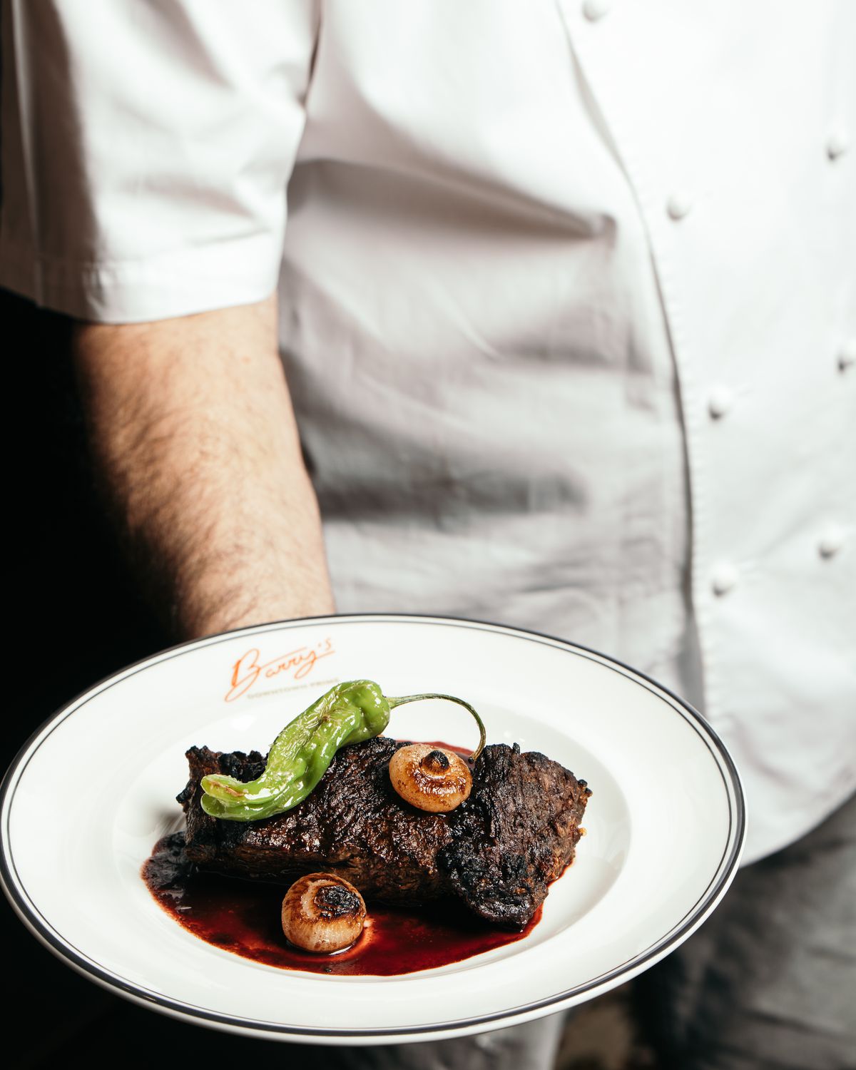 A chef holds a steak on a white plate. 