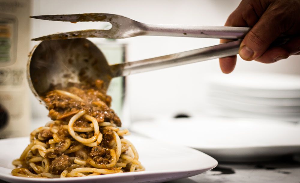 A chef’s hands are seen dispensing a pile of meat-filled pasta on a plate