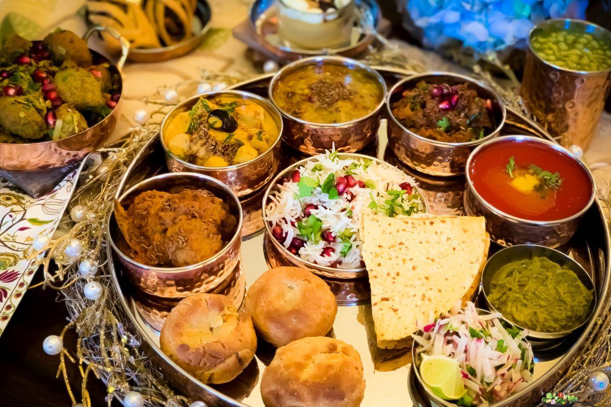 A large platter holding colorful small bowls of food and sauces, plus breads and rice