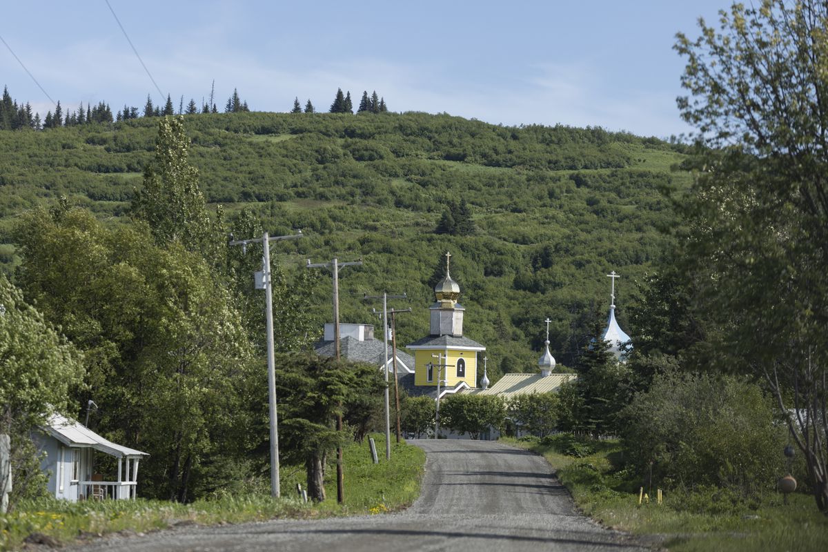 A yellow building with a gold domed roof pops up among green hills and a gravel road. 