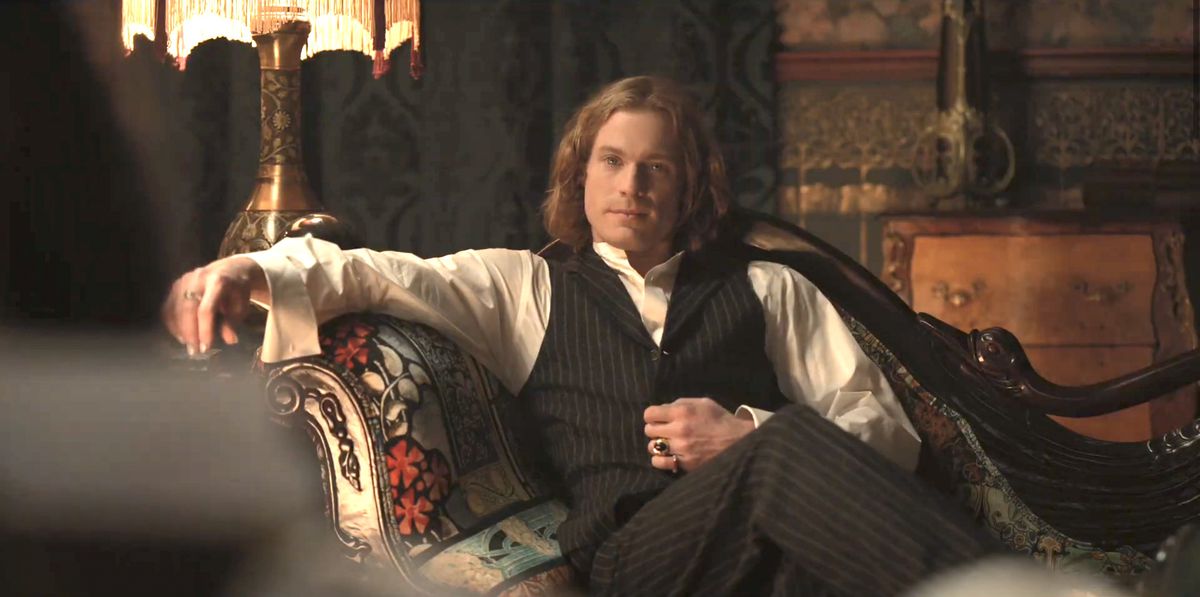lestat lounging in an ornate armchair next to a victorian lamp during an interview with a vampire