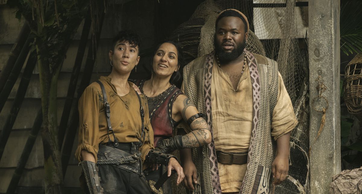 Jim (Vico Ortiz), Archie (Madeleine Sami), and Olu (Samson Kayo) all stand together outside in the Republic of Pirates, reacting with smiles or shock to something offscreen in season 2, episode 7 of Our Flag Means Death