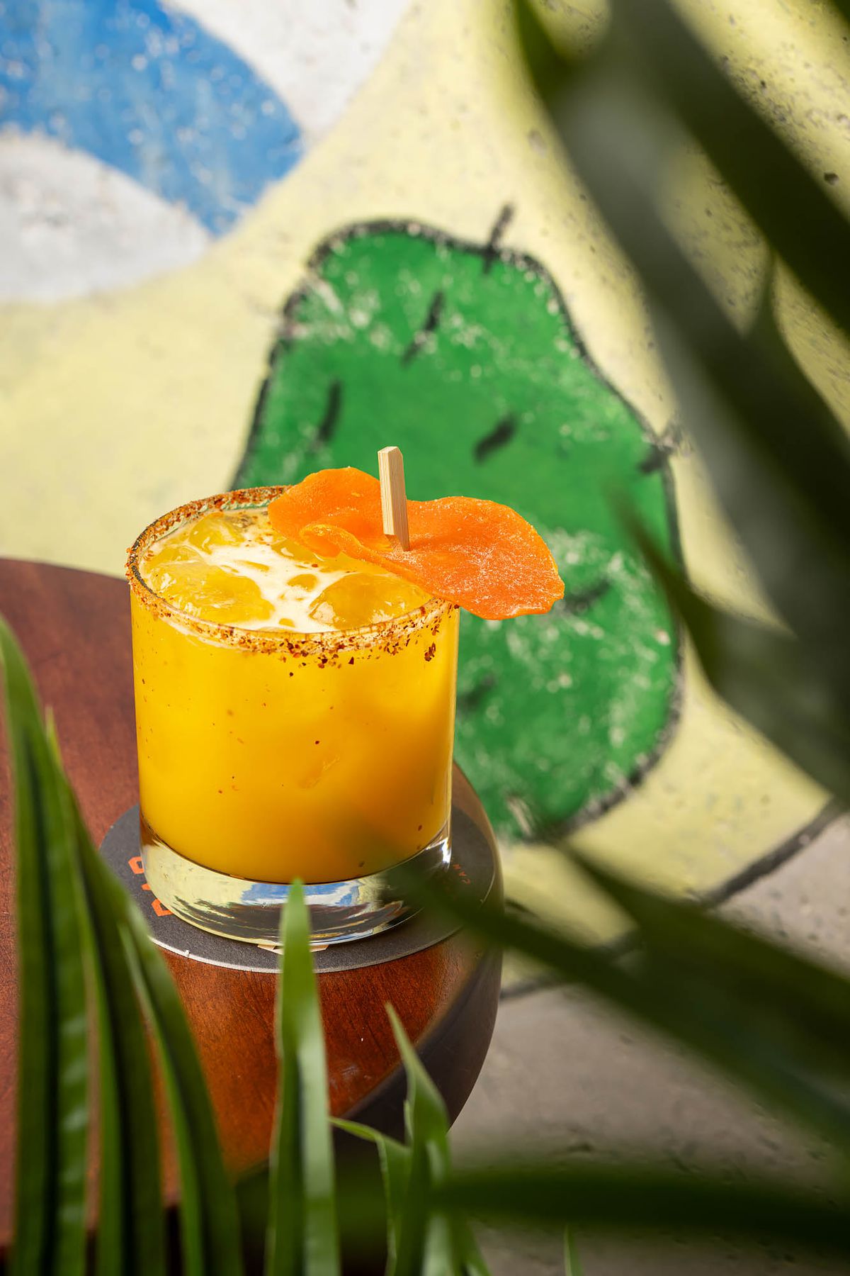 A bright orange mango mezcal margarita with a printed background at Bar CDMX.