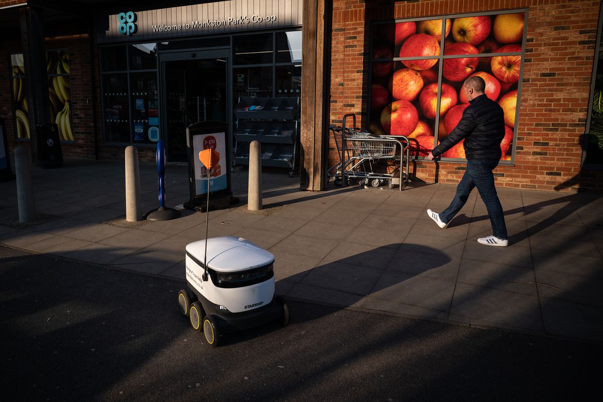 A delivery robot drives by a man walking.
