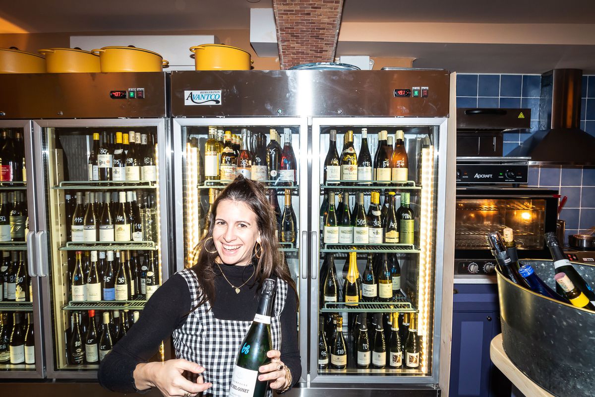 A woman holding a bottle of Champagne is pouring behind a bar.