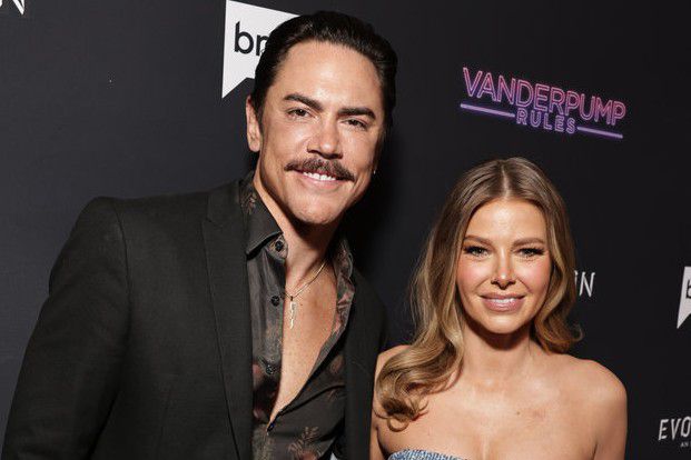 Tom Sandoval and Ariana Madix smile at the camera on a red carpet for the Vanderpump Rules season 10 premiere party.