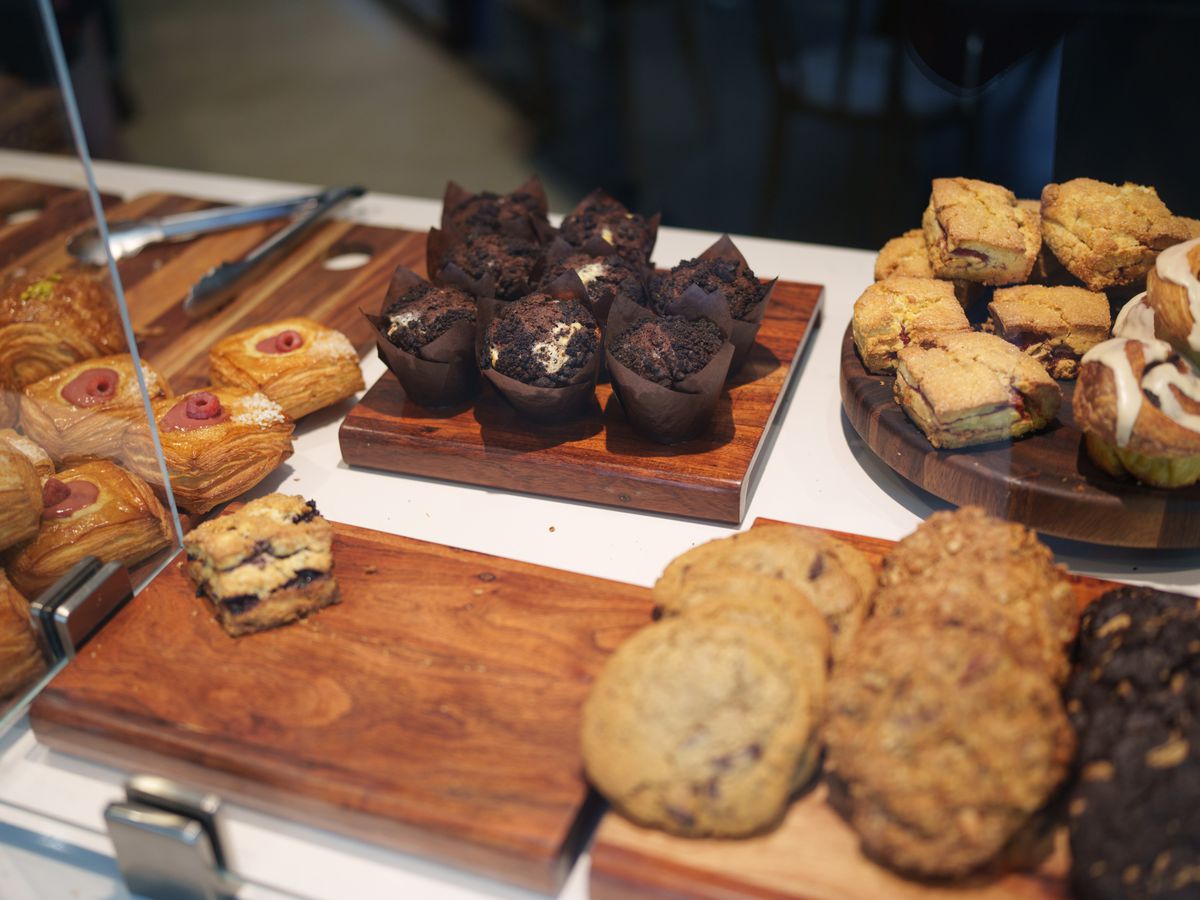 An assortment of pastries on wooden blocks on a white counter behind glass.