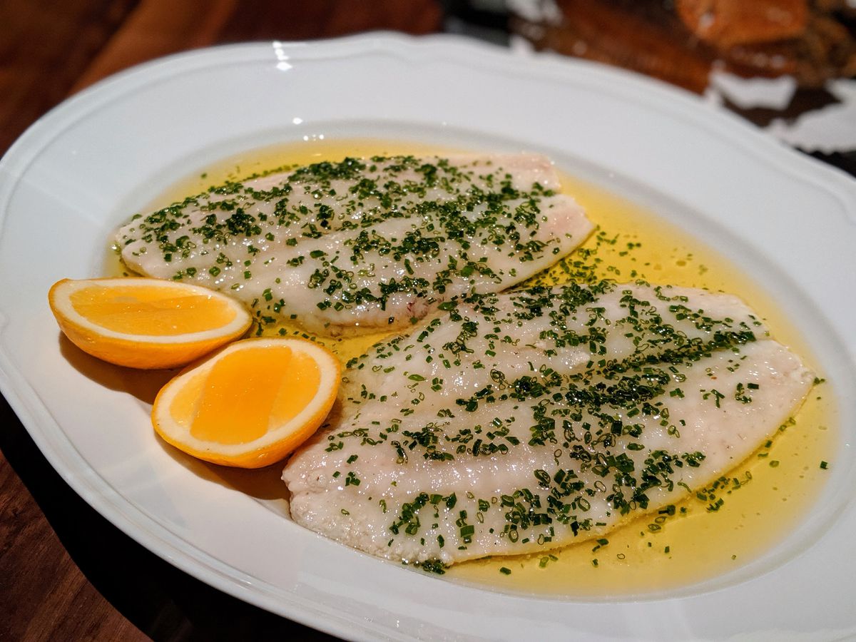 Two fish filets in a pool of butter on a white plate.