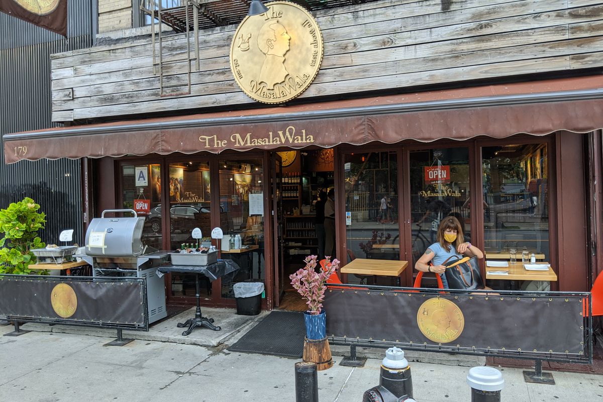 A broad brown storefront with a single customer sitting at a table with a mask.