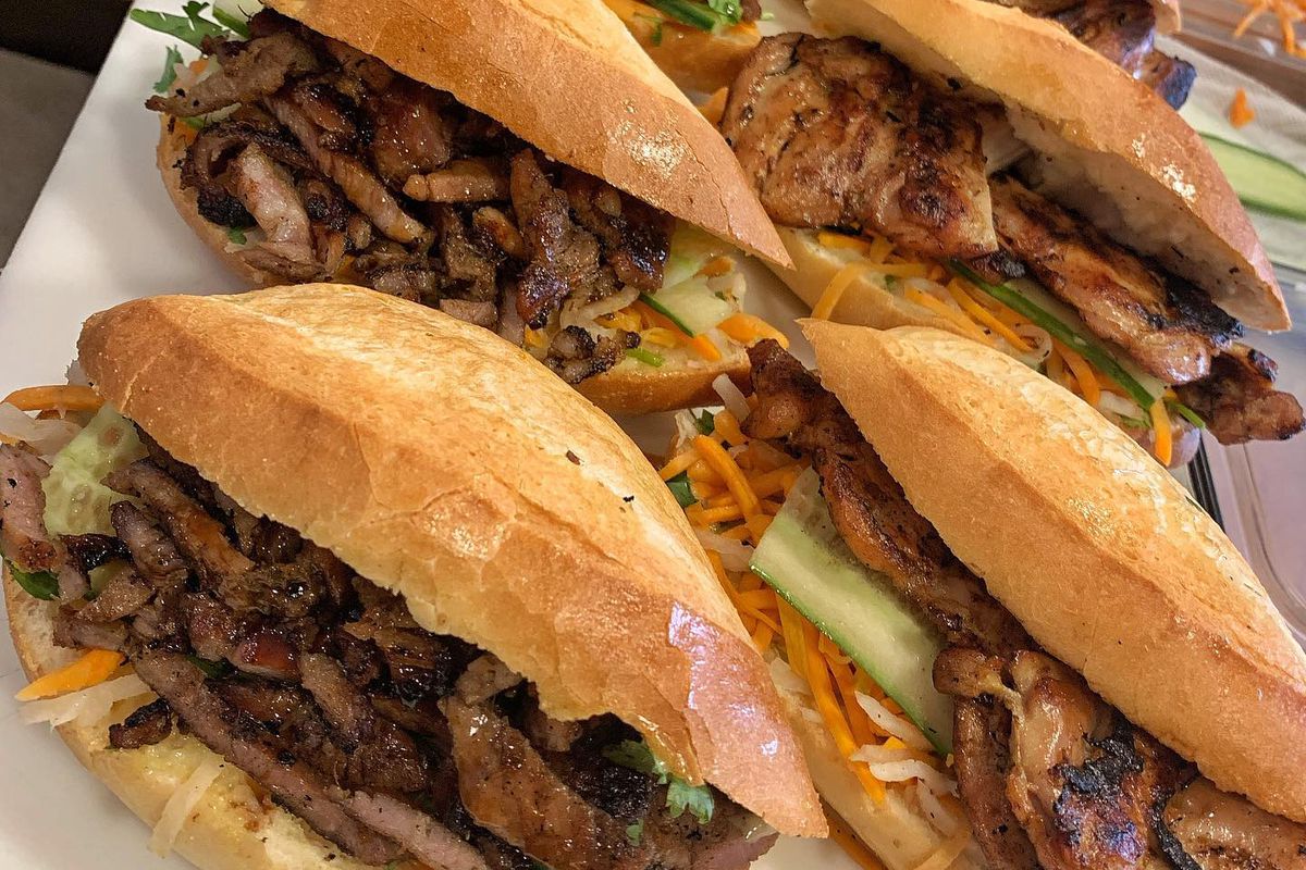Two rows of banh mi sandwiches with grilled meat and fresh vegetables. 