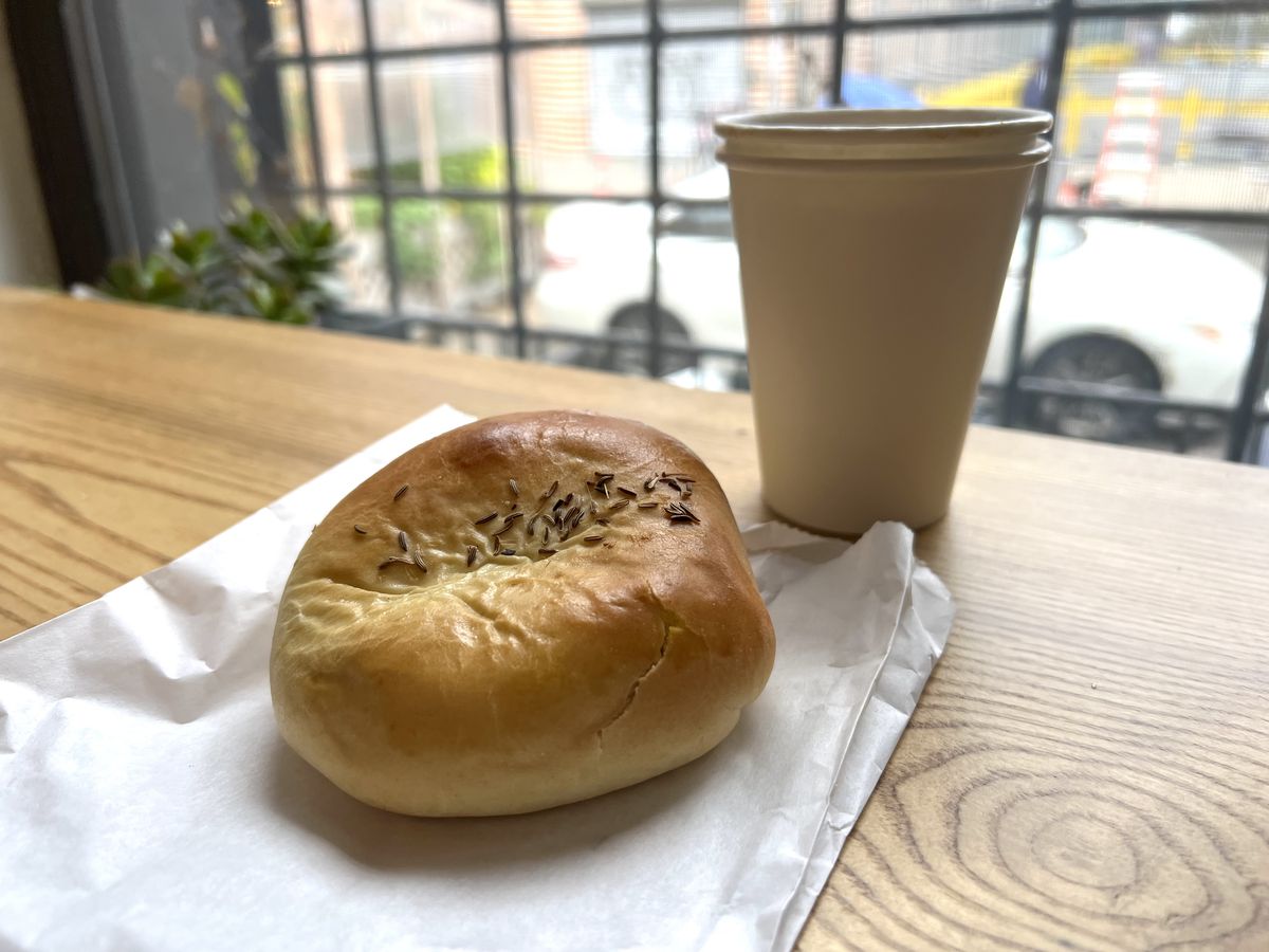 A pirashki sits on a paper bag next to a white cardboard cup of coffee
