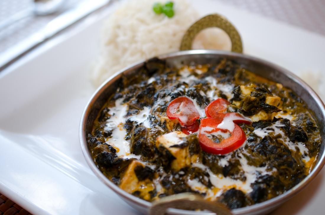 A metal dish of saag paneer in a tray beside a pile of rice