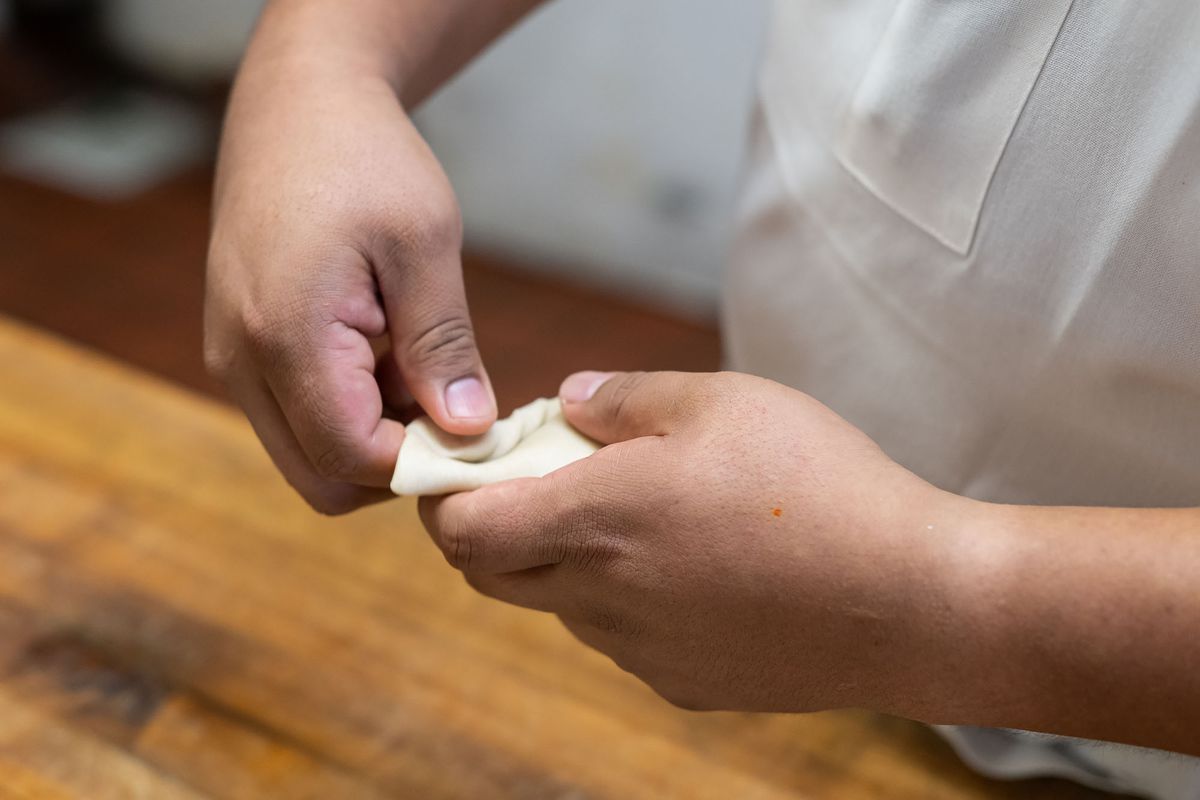 Pora rankų apdoroja empanados kraštus, kad ją uždarytų.
