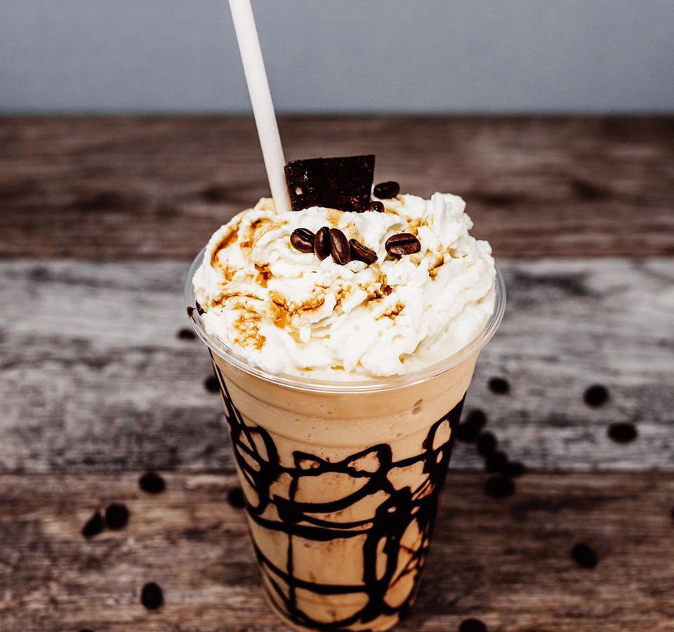 Chocolate milkshake with whipped cream, chocolate drizzle, and other toppings on a wooden counter