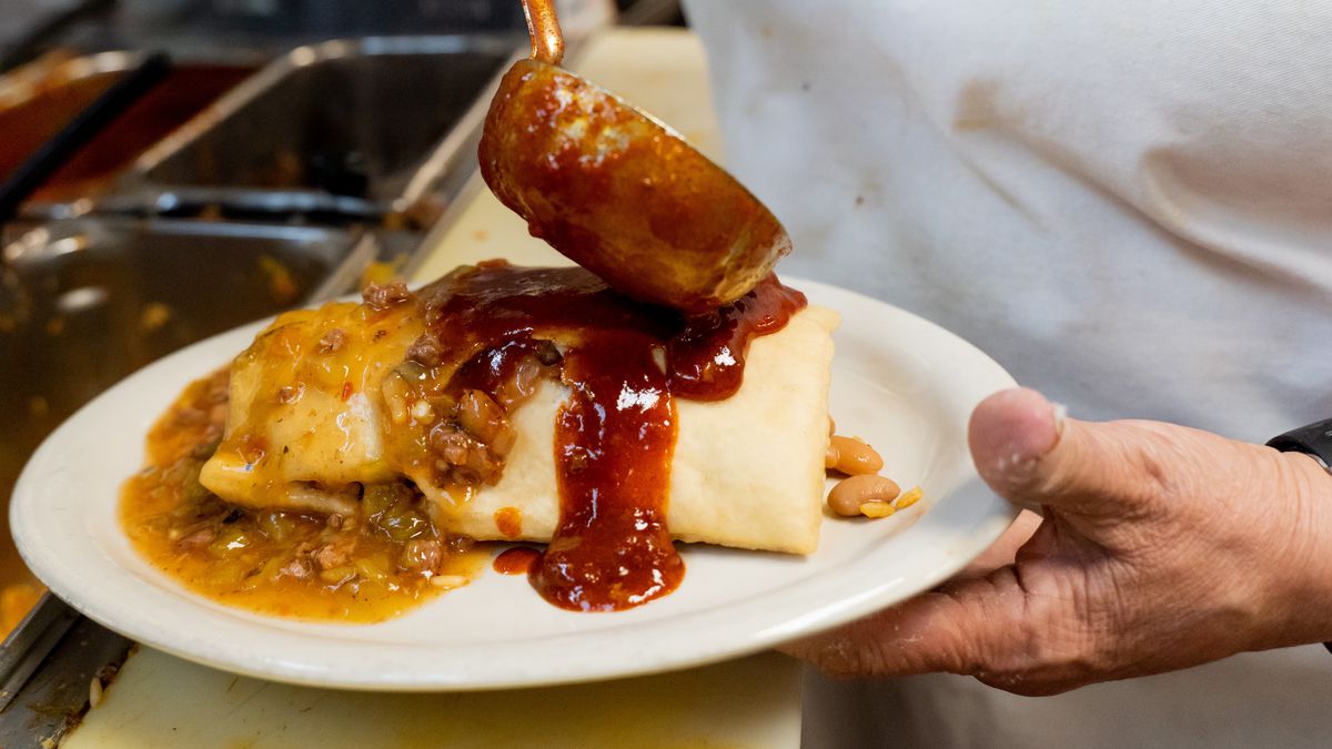 A cook ladles chile on top of a sopaipilla bursting at the seams.