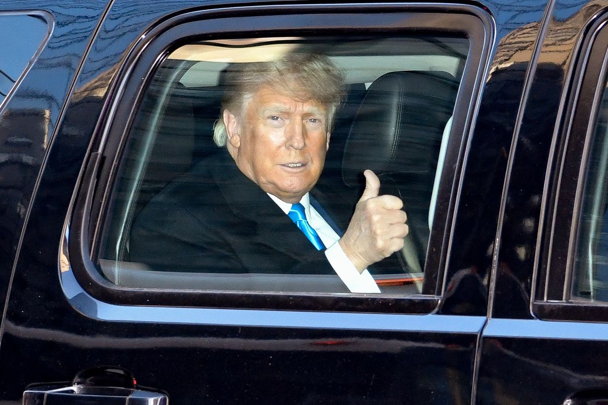 Donald Trump, sitting inside a limousine, makes a thumbs-up gesture through the closed window.