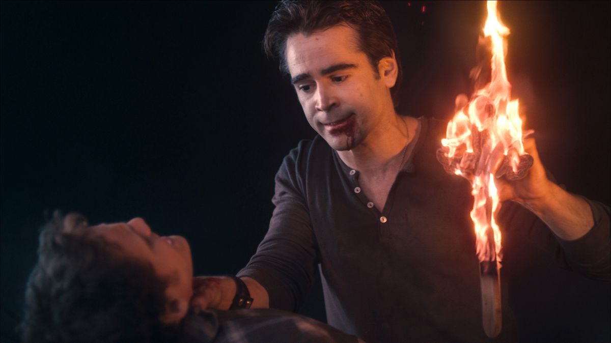 A man (Colin Farrell) with blood dripping from his mouth as he chokes a man on the hood of a car with one hand while clutching a burning cross with his other hand.