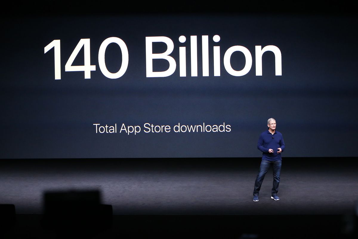 Apple CEO Tim Cook onstage at an Apple event in front of a large screen that reads “140 billion total app store downloads.”