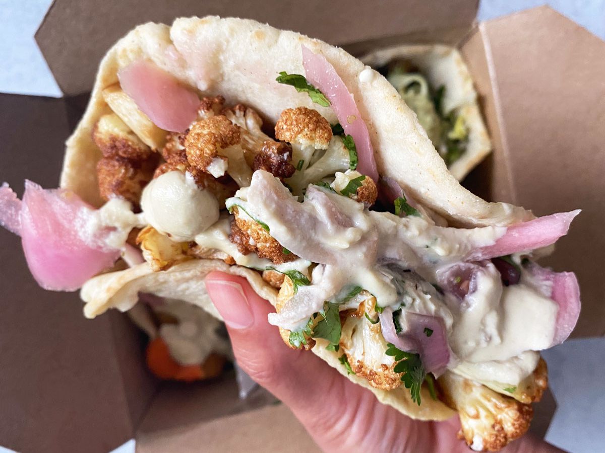 A photo of a hand holding a vegan taco filled with cauliflower, pickled red onions, and cashew crema from Tacovore