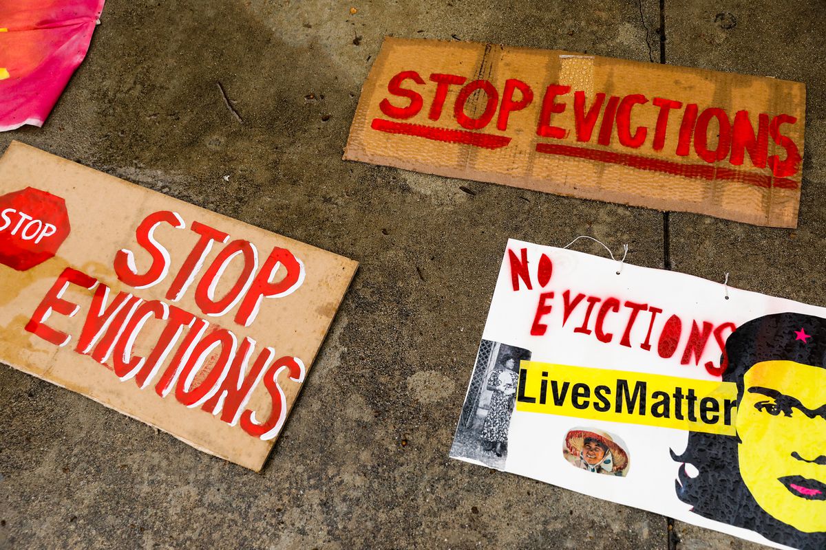 Cardboard signs reading “Stop Evictions” and “No Evictions,” with red stop signs and letters, are laid flat on concrete.